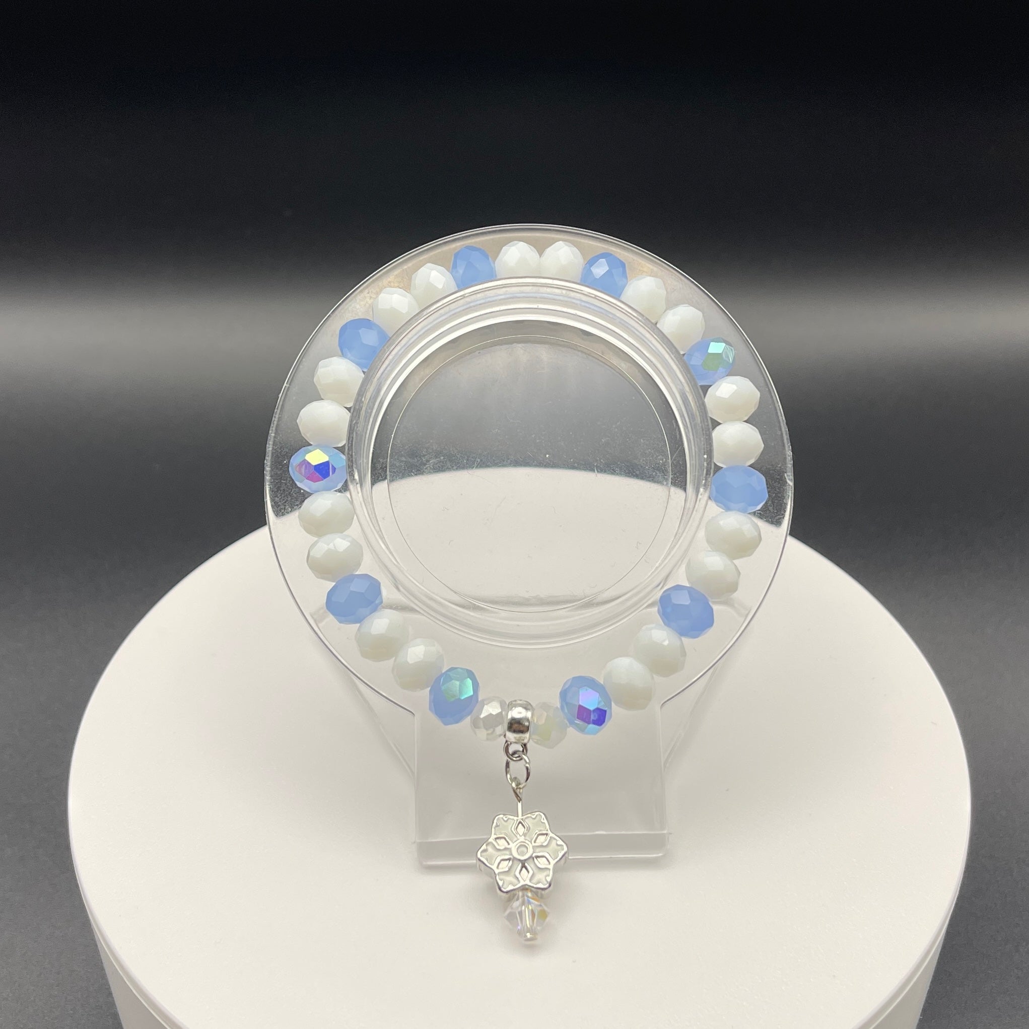 blue and white bead bracelet with a silver snowflake charm on a clear stand against a dark background