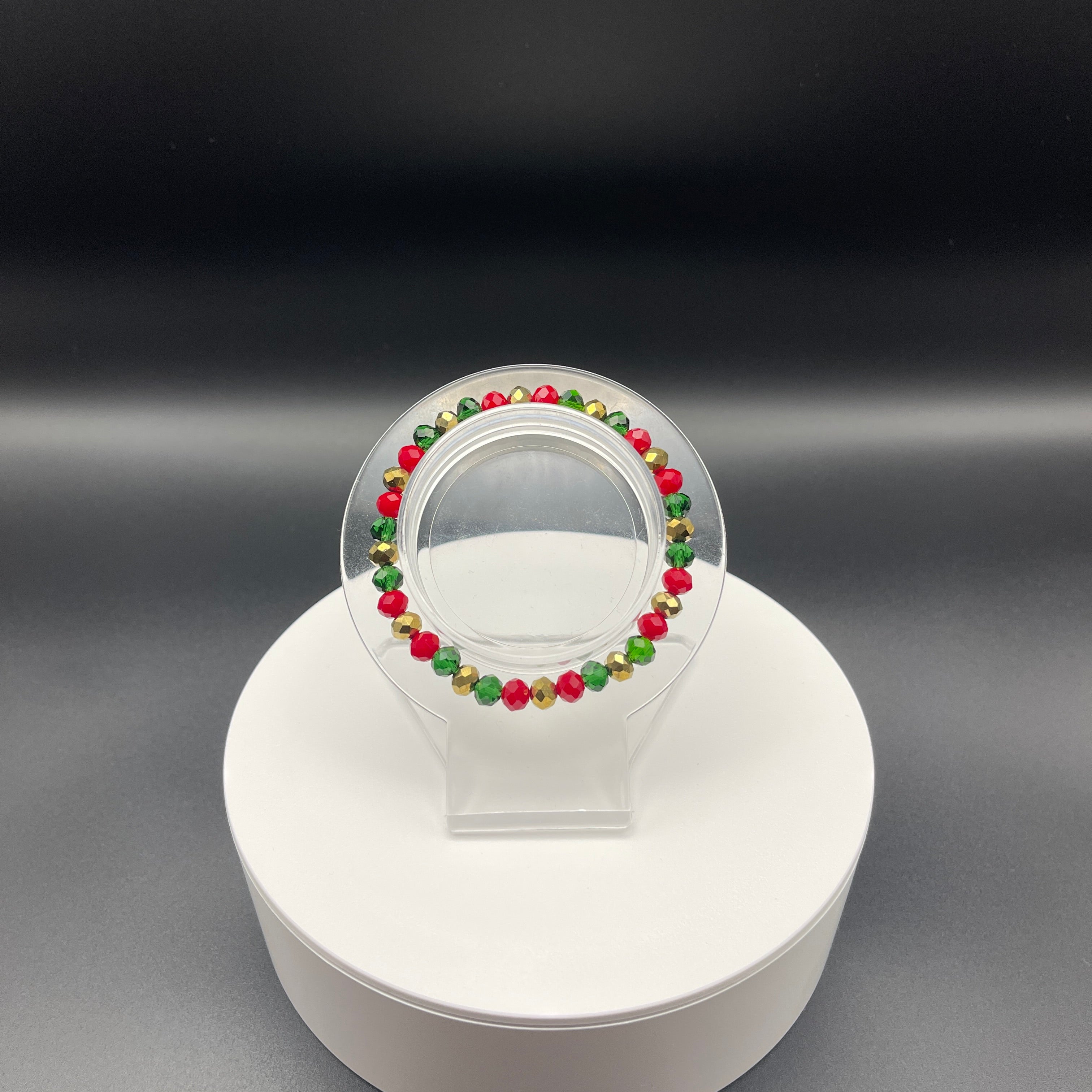 Bracelet with red, green, and gold beads on a clear stand against a dark background