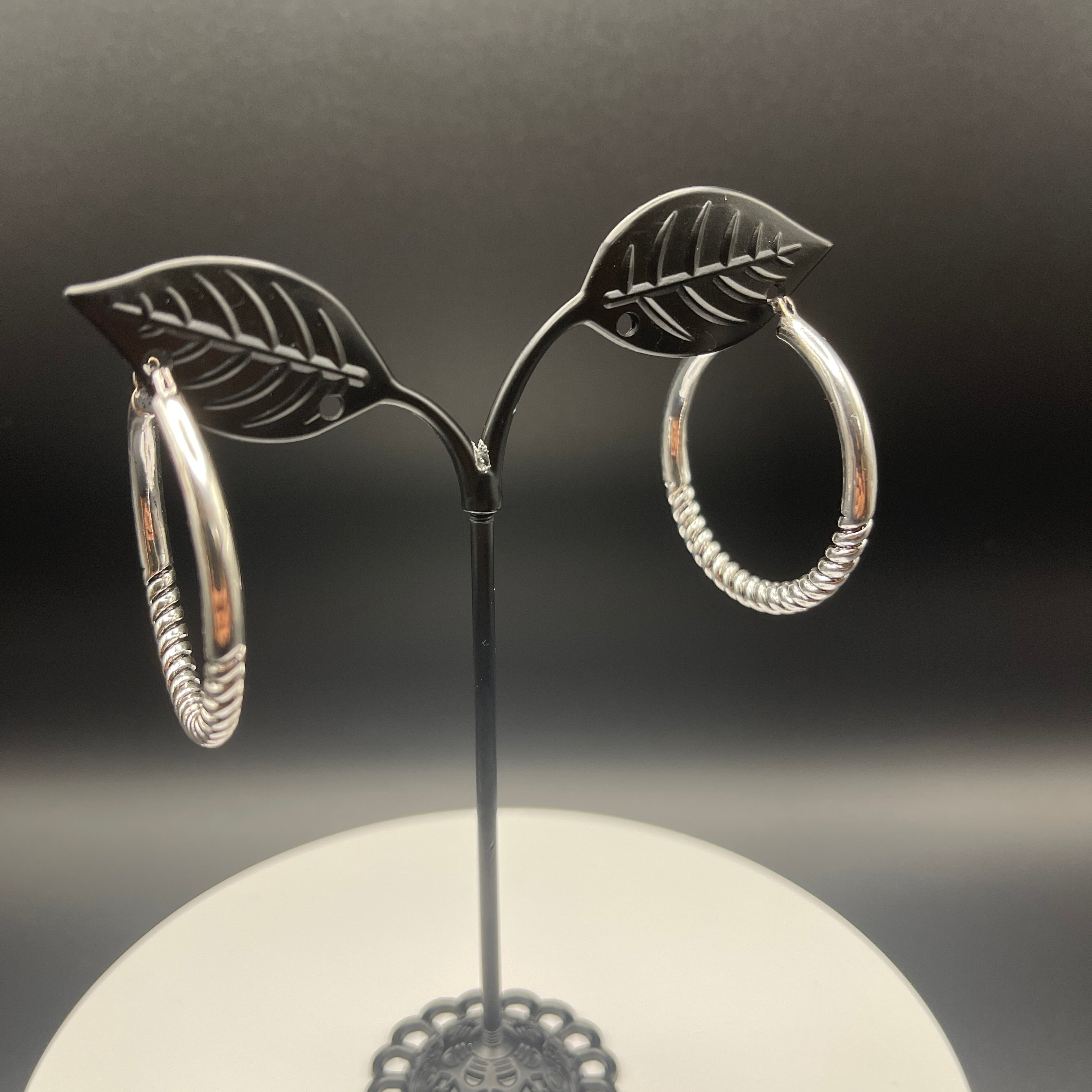 Silver hoop earrings on a black stand with a dark background