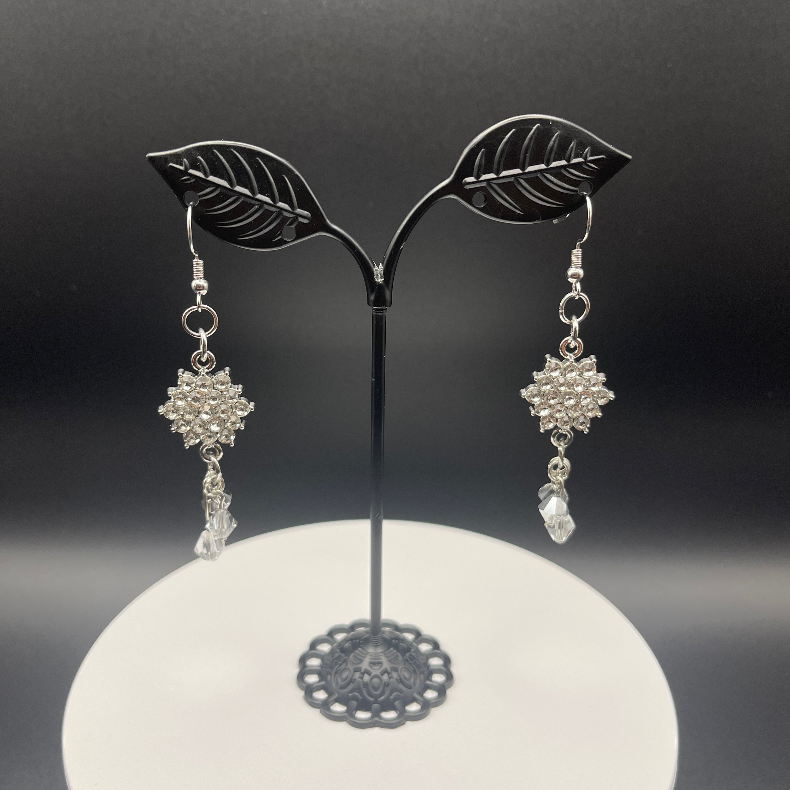 Silver and rhinestone star-shaped earrings on a black and white stand against a dark background